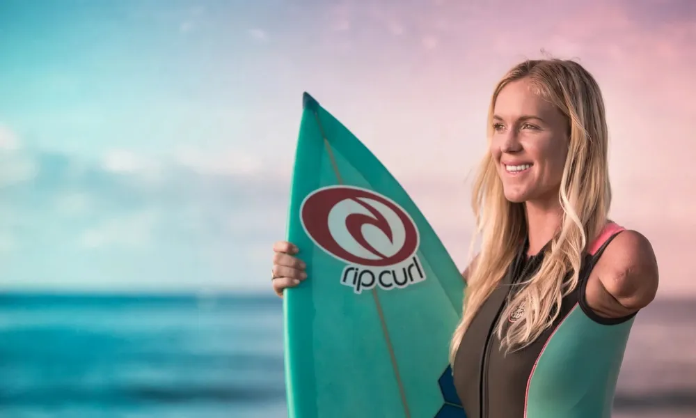 Bethany Hamilton holding her custom surfboard to competitive surfing-Real Life Inspiring Stories