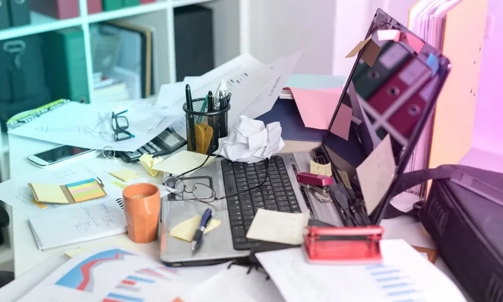 A cluttered desk featuring a laptop, papers, notes, and a coffee mug-Gen Z Slang