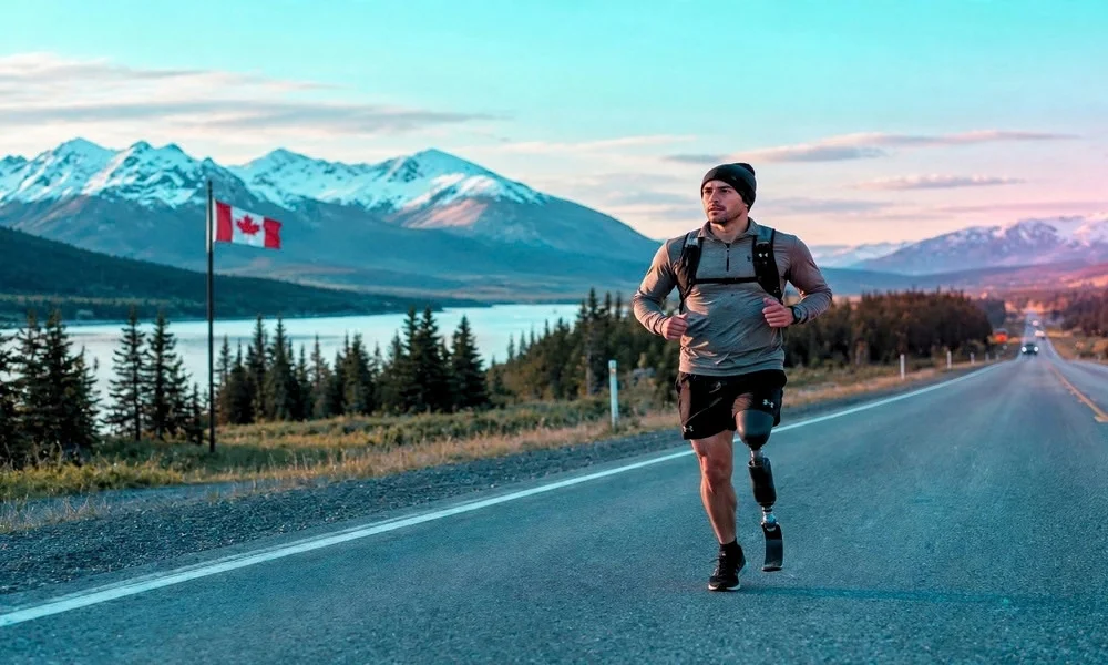 An athlete with a prosthetic leg running along an open highway with mountains in the background.