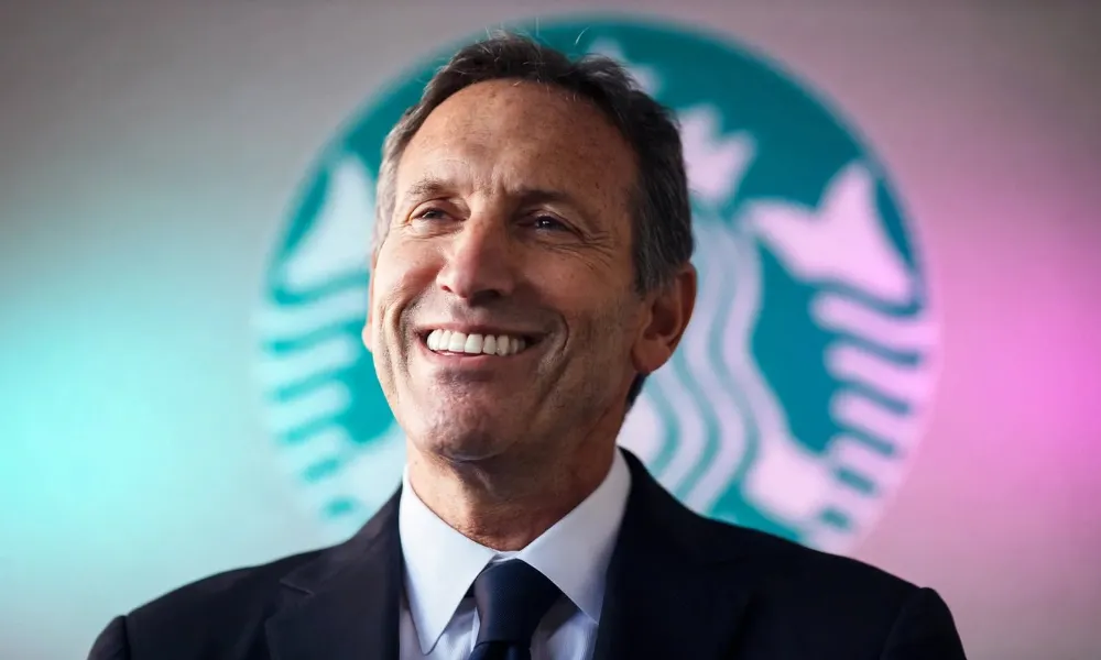 Howard Schultz smiling in front of a green Starbucks logo background