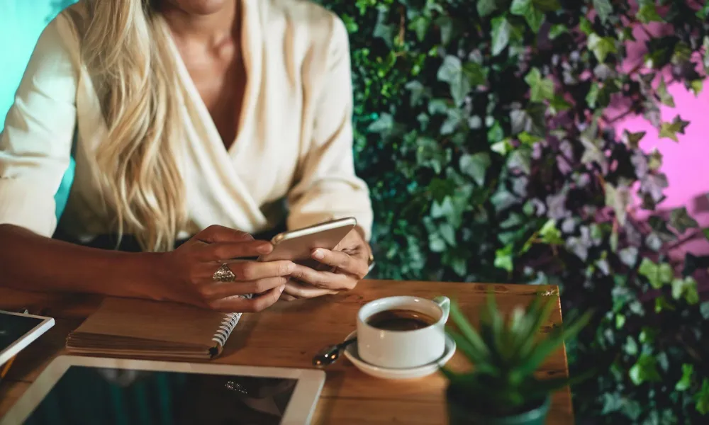 A person looking at a smartphone screen while sitting at a wooden table with a cup of coffee.