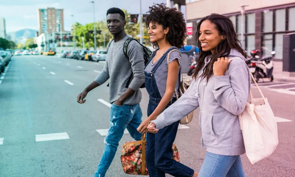 Three stylish friends walking together down a city street with bags and backpacks.