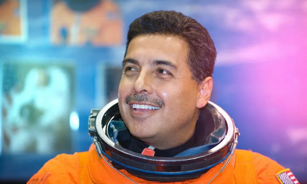 José Hernández smiling in an orange NASA space suit with his helmet collar fitted.