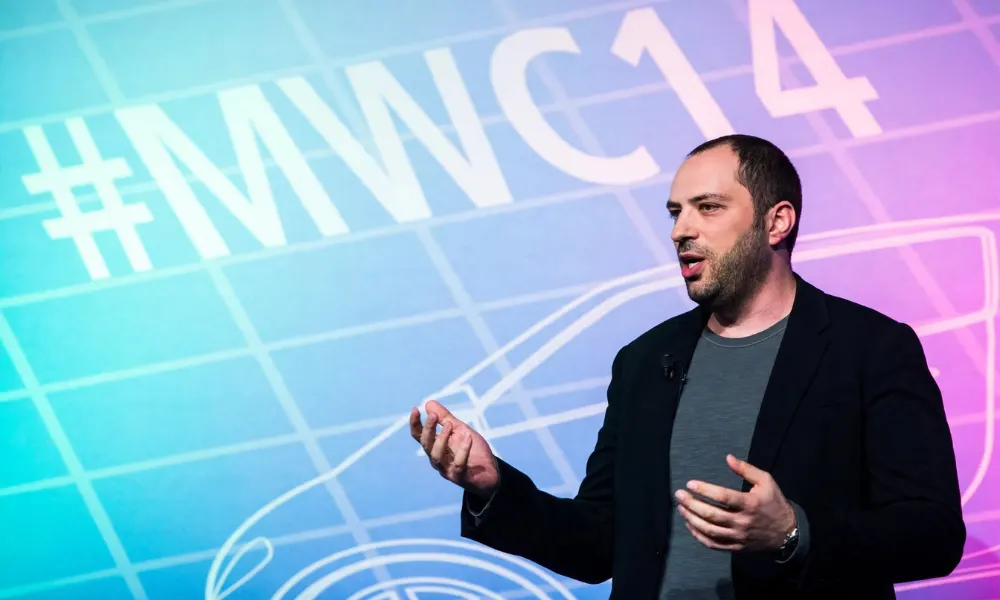 Jan Koum gesturing while presenting on stage at a technology conference.